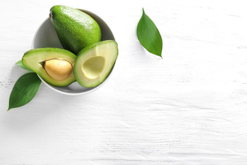 Bowl with ripe avocados on white wooden background