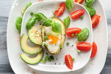 Tasty baked avocado with egg and fresh vegetables on plate, closeup
