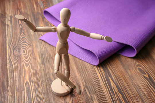 Yoga mat and small mannequin on wooden background