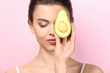 Beautiful young woman with avocado on color background