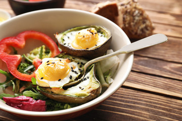 Baked avocado with eggs and vegetables on wooden background, closeup