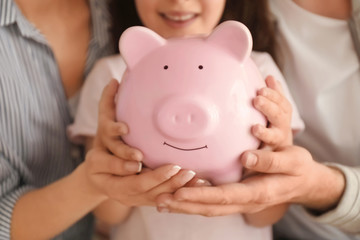 Little girl with her parents  holding piggy bank, closeup. Money savings concept