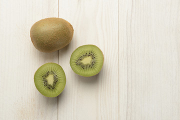 Un kiwi abierto y uno entero sobre fondo de madera blanca