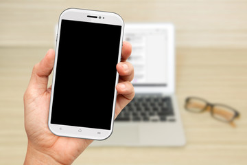 Hand Hold a white Smartphone with laptop background