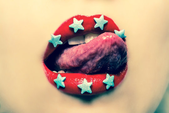 Woman licking her lips painted red lipstick with candy in the form of stars. Vintage, grunge old retro style photo.