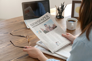 Young woman reading newspaper at table indoors