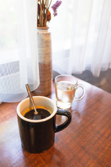 Americano coffee on wooden table near window with sunlight.