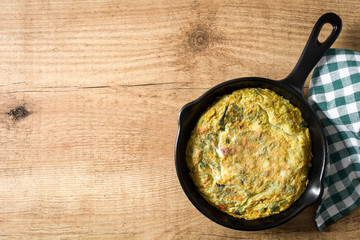 Frittata made of eggs and vegetables in a iron pan, on wooden table. Copyspace