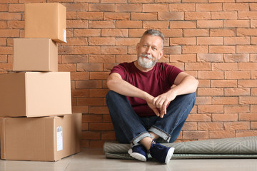 Mature man with moving boxes sitting on carpet at new home