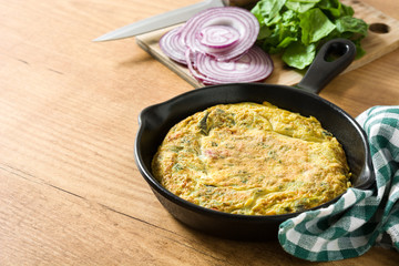 Frittata made of eggs and vegetables in a iron pan, on wooden table. 