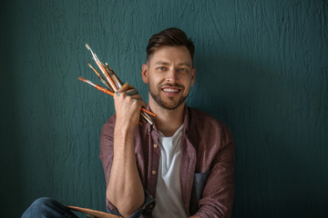 Male artist with paint tools on color background