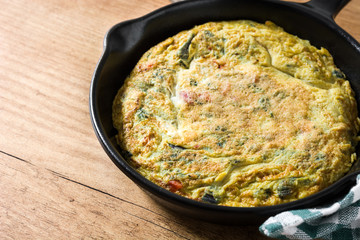 Frittata made of eggs and vegetables in a iron pan, on wooden table. 