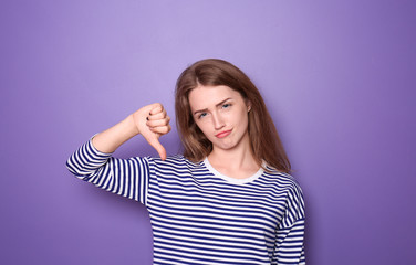 Beautiful young woman showing thumb-down gesture on color background
