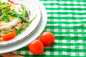 Fried eggs with arugula and tomatoes cherry on white plate and checkered cloth. Copy space