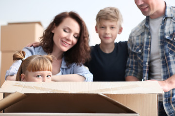 Cute girl in cardboard box and her family indoors. Moving into new house