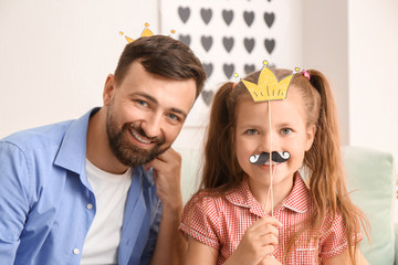 Portrait of smiling father and daughter with artificial mustache and crown at home