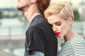 cropped image of stylish girlfriend hugging tattooed boyfriend from back on bridge