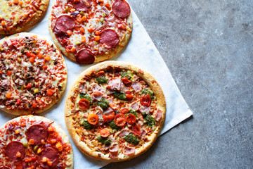 Five fresh backed hot pizzas on white tablecloth on grunge grey table background with copy space for text.