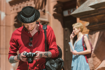man looking at photo camera while girlfriend standing behind
