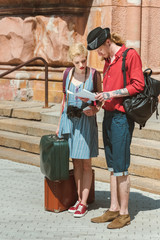 couple of travelers with backpacks and retro suitcases looking at map