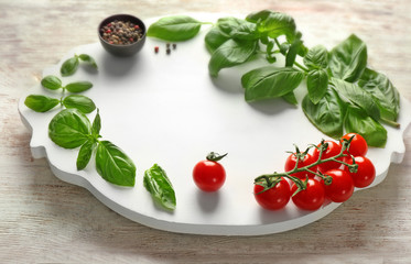 Board with frame made of fresh basil and tomatoes on wooden background