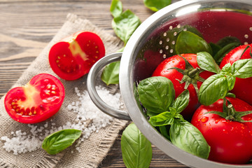 Colander with fresh basil and tomatoes on wooden background, closeup