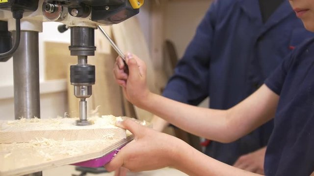 Father and son drills the wooden plank using joinery machine in carpentry workshop