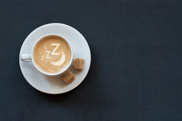 Cup of coffee with milk, cane sugar and zzzzz and moon sign on dark background. Top view. Copy space.