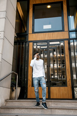 A young man travels through the streets of the city. Boy in sunglasses Stylish man near the building. The man sits on a whip. Beard and hair in a stylish guy.