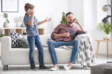 Dad and his little son talking on mobile phones at home