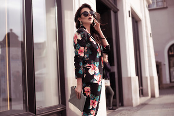 Obraz na płótnie Canvas Fashionable brunette woman holding a smartphone, talking on the phone. ..Dressed in nice clothes, sunglasses walking in the street. Fashion spring summer photo
