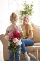 Cute little girl hiding bouquet of flowers for mother behind her back