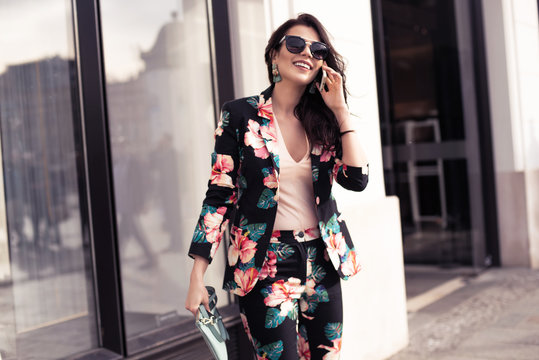 Fashionable brunette woman holding a smartphone, talking on the phone. ..Dressed in nice clothes, sunglasses walking in the street. Fashion spring summer photo