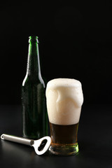 Glass and bottle of cold beer with opener on dark background