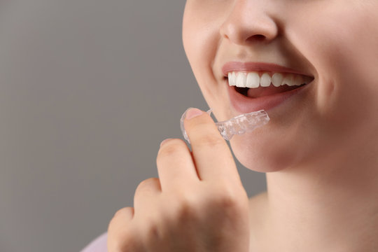 Woman putting occlusal splint in mouth on grey background, closeup