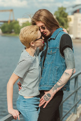 Fototapeta na wymiar boyfriend with tattoos and stylish girlfriend hugging and going to kiss on bridge