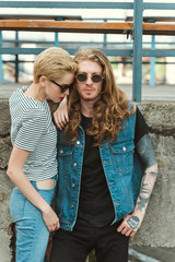 boyfriend with tattoos and stylish girlfriend posing in sunglasses near bridge