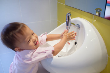 Cute little Asian 18 months / 1 year old toddler baby boy child washing hands by himself on white sink and water drop from faucet, Sanitation / hygiene concept, Selective focus at water tap