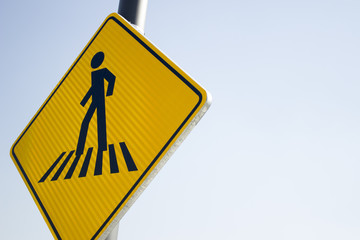 Yellow pedestrian street sign hung in a pole under a shiny sun.