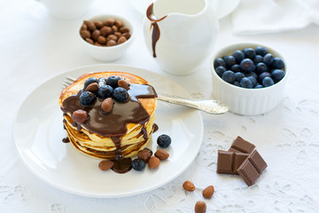 Traditional breakfast concept. Stack of pancakes with chocolate sauce, blueberries and nuts on white table cloth. Selective focus