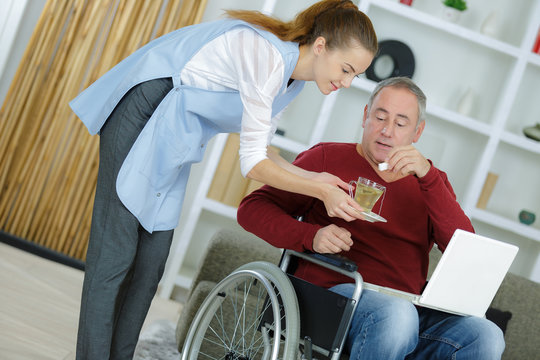 female assistant giving a cup of coffee to disabled male