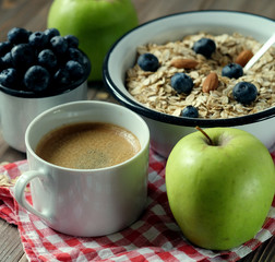 A healthy breakfast is a great start to a new day. Oatmeal porridge, coffee, apple, berries and nuts on a wooden table.
