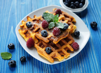 Belgian waffles with blueberries, raspberries and powdered sugar on wooden table.