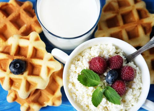Cottage cheese with berries, waffles and milk on a wooden blue background.