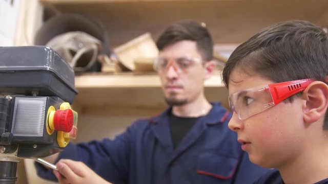 Teenager boy with his dad drills the wooden plank using industrial joinery machine in workshop