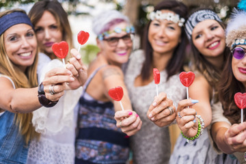 group of mixed ages women from young to old stay together in friendship taking and offering a candy hearth lollypop to you. peaceful and lifestyle inspired to peace and love like hippy style