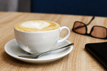 White cup of cappuccino with latte art on wooden table. Shallow focus.