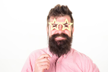 Hipster with beard and mustache on cheerful smiling face posing with star shaped glasses, copy space. Man holds party props star shaped eyeglasses, white background, close up. Superstar concept