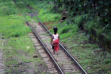 Behind of Myanmarese lady villager walking on the railroad tracks and put the black bag or belongings on the head.