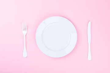 Concept minimal .Time to Eat.  Fork, knife and white Plate on a pink pastel Background. Top View....